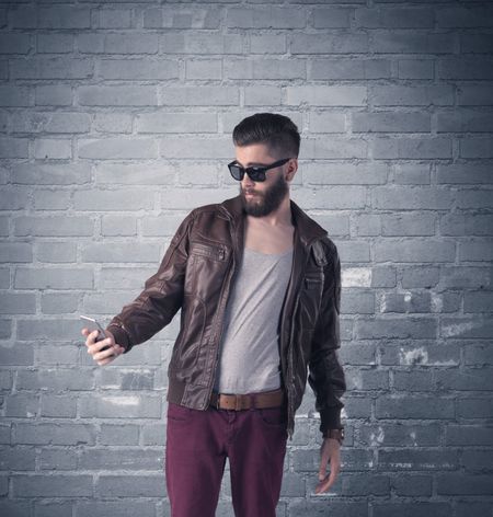 stylish-hipster-guy-beard-sunglasses-standing-428242609 A stylish hipster guy with beard and sunglasses standing in casual clothes in front of an urban blue brick wall background concept