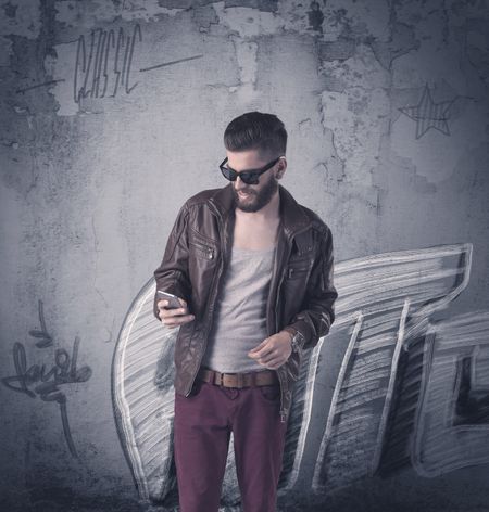 A handsome hipster guy with beard and sunglasses standing in front of an urban wall with graffiti concept
