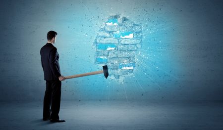 Business man hitting grungy brick wall with huge hammer