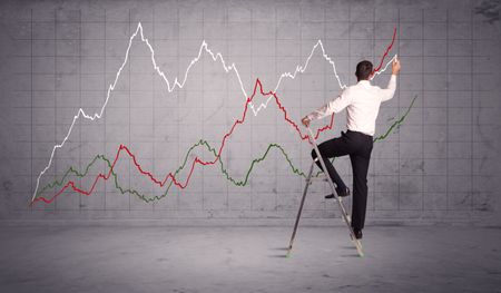 A guy in modern suit standing on a small ladder and drawing a chart on grey wall background with exponential progressing curves, lines