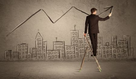 A man in elegant suit standing on a small ladder and drawing a line on brown wall background with buildings