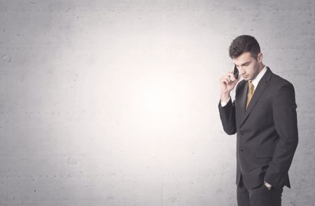 Young sales business person in elegant suit standing in front of clear empty grey wall background while talking on the phone