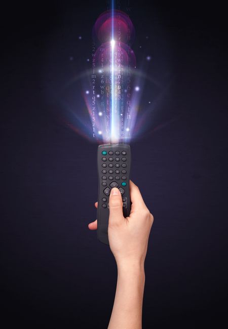 Hand holding a remote control, shining numbers and letters coming out of it
