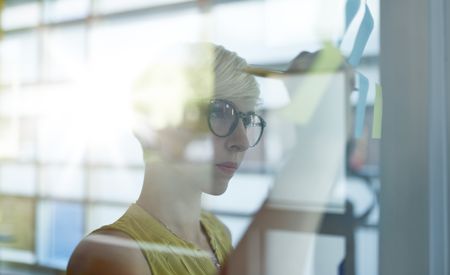 Two creative millenial small business owners working on social media strategy brainstorming using adhesive notes in windows