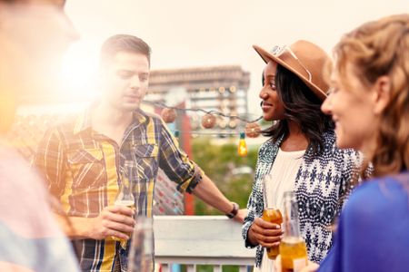 Multi-ethnic millenial group of friends partying and enjoying a beer on rooftop terrasse at sunset