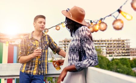 Multi-ethnic millenial couple flirting while having a drink on rooftop terrasse at sunset