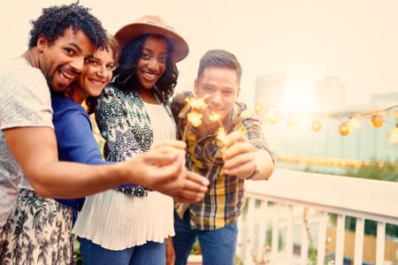 Multi-ethnic millenial group of friendsfolding sparklers on rooftop terrasse at sunset