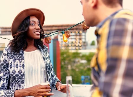 Multi-ethnic millenial couple flirting while having a drink on rooftop terrasse at sunset