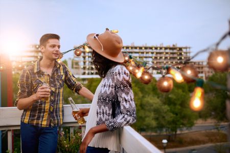 Multi-ethnic millenial couple flirting while having a drink on rooftop terrasse at sunset