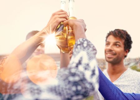 Multi-ethnic millenial group of friends partying and enjoying a beer on rooftop terrasse at sunset