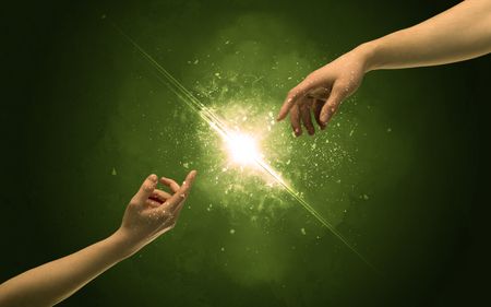 Two naked male hands about to touch, lighting the spark with modest explosion in front of green background concept