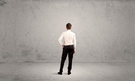 A confused sales person having a dilemma, standing with his back in empty grey urban environment concept