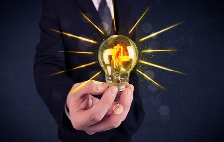 A male business person holding an electric light bulb in his hand with beam rays illustration concept.