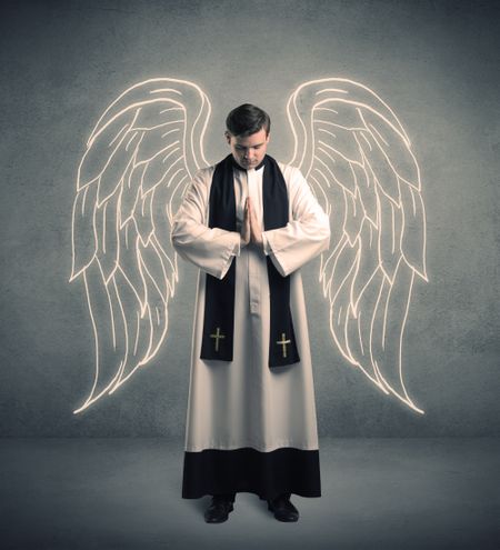 A young male priest with drawn large angel wings standing with the holy bible in his hands concept.