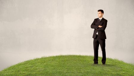 A successful caucasian elegant business man standing in small green grass with briefcase in front of clear empty background concept.