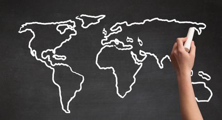 A teacher drawing the map of the world on a blackboard with a chalk