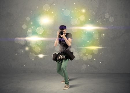 A young amateur photographer with professional camera equipment taking picture in front of grey wall full of colorful bokeh and glowing lights concept