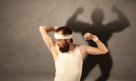 A funny young guy posing in front of brown background with musculous body shadow reflected on the wall 