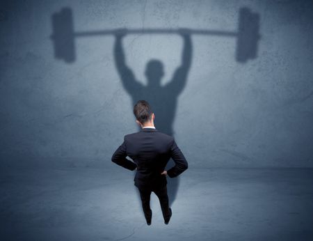 A confident young elegant salesman with briefcase facing a wall, looking at his strong, weight lifting shadow concept