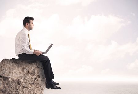 A young sales person in elegant suit sitting with paper on top of a stone in the clouds concept