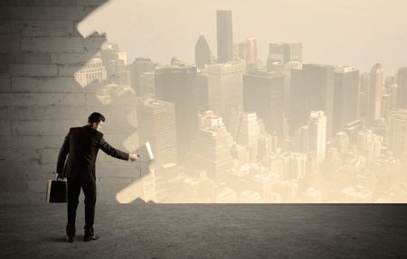 An elegant businessman with a paint roller transforming a brick wall into urban city landscape including tall buildings concept