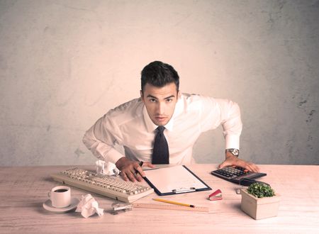 A young office worker sitting at desk working with keyboard, papers, highliter in front of empty clear background wall concept