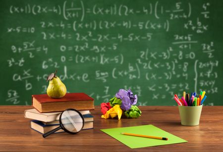 Back to school concept with long numbers calculation on blackboard and a desk with books, fruit