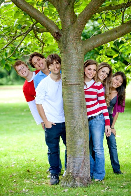 Happy friends at the park hiding behind a tree