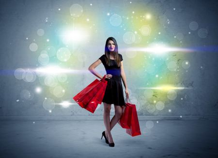 A beautiful young girl standing with long hair and red shopping bags in front of colorful light bokeh urban wall background concept