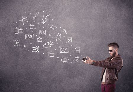 An elegant hipster guy trying to use a vintage camera with camera settings icons drawn on wall, like flash, white balace or ISO value concept