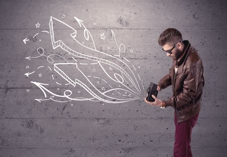 A hipster guy opening his point of view through looking a vintage camera concept with illustratied drawn arrows on urban wall