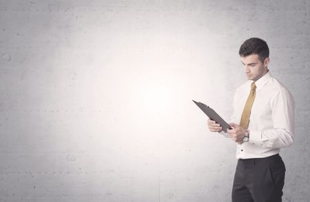 Young sales business person in elegant suit standing in front of clear empty grey wall background while talking on the phone