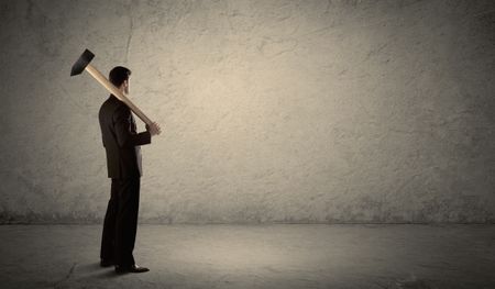 business-man-standing-front-grungy-copyspace-457368736 Business man standing in front of a grungy copyspace wall with a hammer