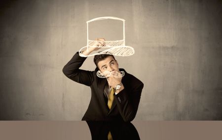 A young happy businessman in elegant suit drawing funny hat and mustache in empty grey space with a chalk illustration concept