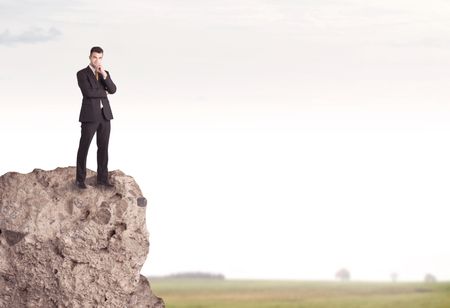 A successful good looking business person standing on top of a high cliff above country landscape with clear white sky concept