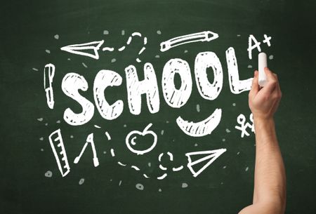 A teacher writing school, drawing children things on clean green chalkboard by hand