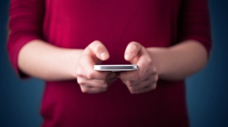 Young woman holding smarthphone in hand while typing