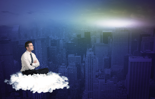 Caucasian businessman sitting on a white fluffy cloud above the city, thinking and wondering