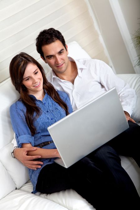 Beautiful couple with a laptop sitting on a coach indoors