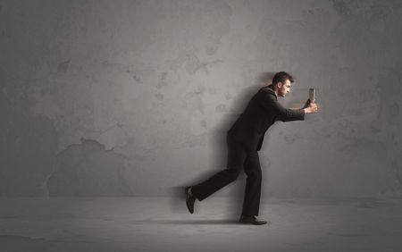 Running businessman in a rush with device in hand on background