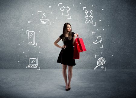 A beautiful young girl in black standing with red shopping bags in front of urban wall background and laptop, shoes, tennis icons concept