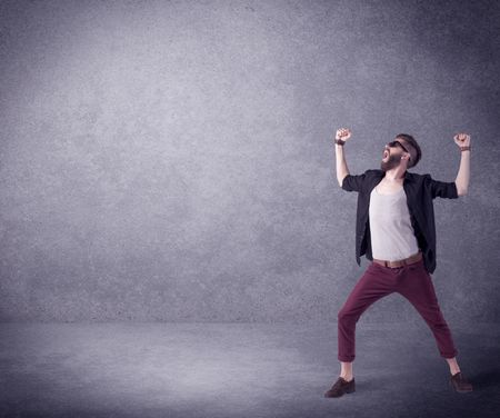 A hipster guy in stylish clothes shouting in front of an empty urban concrete wall background concept