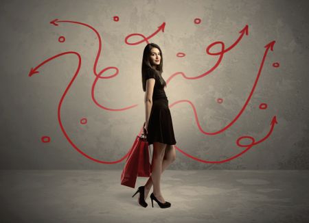 An elegant young lady in black holding red shopping bags in front of urban wall background with drawn red arrows and circles concept