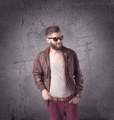 A hipster fashion model guy in casual clothing stnading with mobile phone in front of concrete urban wall background concept