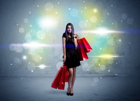 A beautiful young girl standing with long hair and red shopping bags in front of colorful light bokeh urban wall background concept