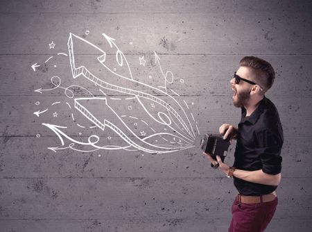 A hipster guy opening his point of view through looking a vintage camera concept with illustratied drawn arrows on urban wall