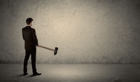 Business man standing in front of a grungy copyspace wall with a hammer