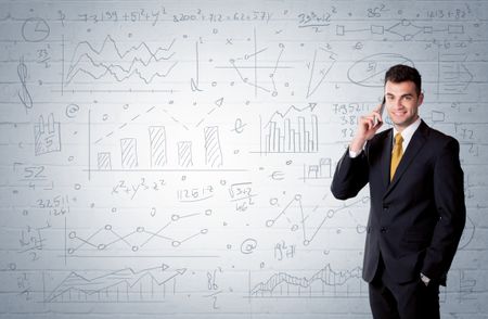 A confident young businessman standing in front of wall with drawn pie charts, graphs, numbers, arrows concept