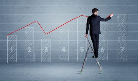 A man in elegant suit standing on a small ladder and drawing a chart on blue wall background with numbers, lines, blocks,