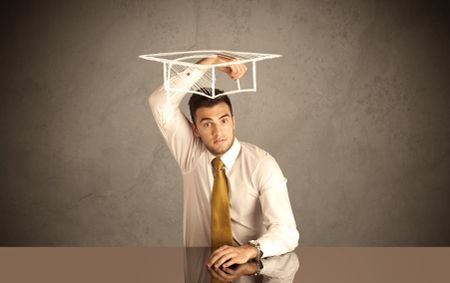 An elegant, successful university student drawing himself a square academic mortarboard cap with a chalk in front of grey wall background concept